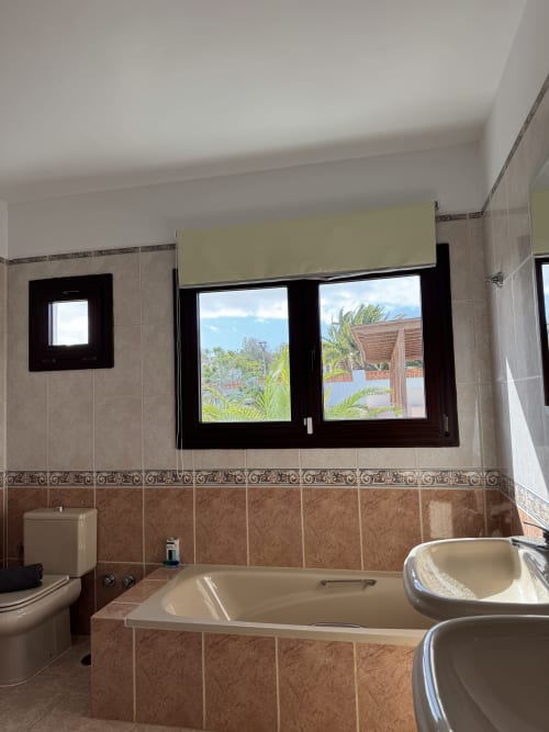 Baño moderno con vista al jardín en villa Kamalahouse en Corralejo con bañera y ventanales panorámicos
