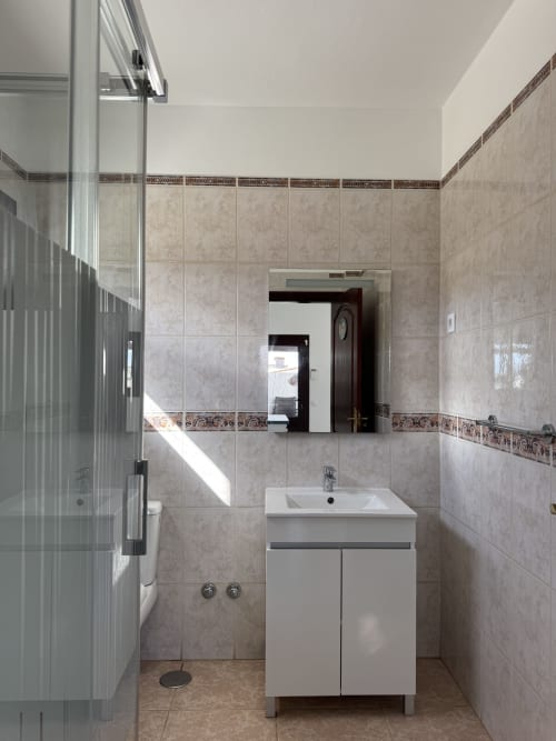 Baño moderno en la villa Kamalahouse de Corralejo con vanidorio blanco, azulejos beige y ducha de cristal