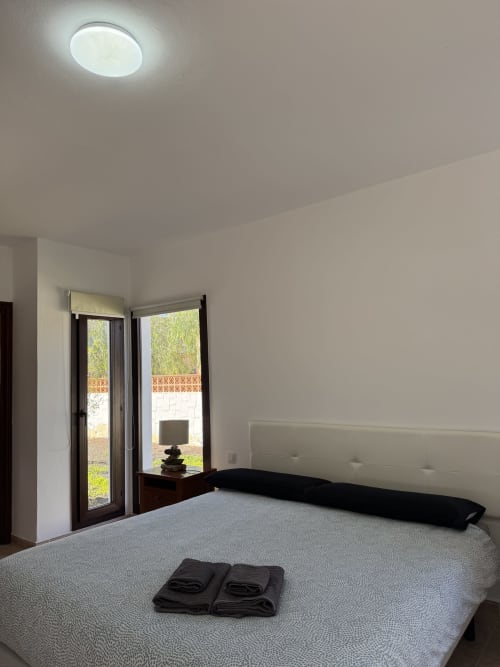 Dormitorio de villa moderna en Corralejo con vista al jardín, lámpara de techo blanca, puertas francesas y decoración minimalista