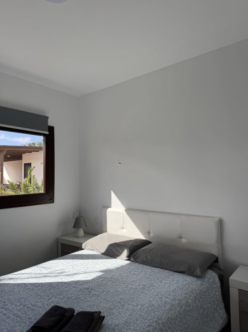 Dormitorio de villa moderna con vista al jardín en Corralejo, ropa de cama blanca y decoración minimalista