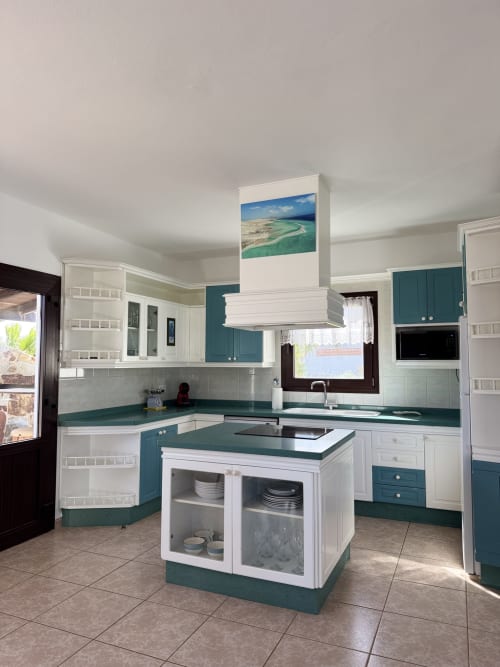 Cocina moderna con muebles en azul turquesa y blanco, isla central y fotografía costera en villa Kamalahouse, Corralejo