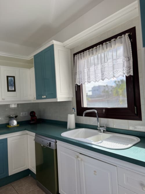 Cocina moderna de villa en Kamalahouse con encimeras color turquesa, gabinetes blancos y vista al jardín desde la ventana