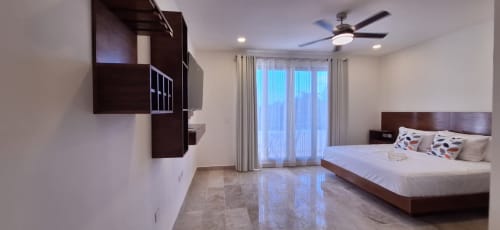 Spacious Itzamná Suite Deluxe bedroom in Playa del Carmen with king bed, dark wood furniture, ceiling fan, and modern