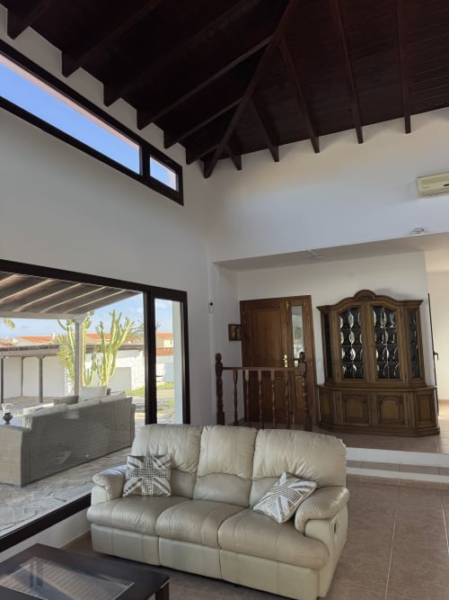 Sala de estar moderna en villa de Corralejo con sofá crema, vigas vistas y vistas al jardín a través de puertas de cristal