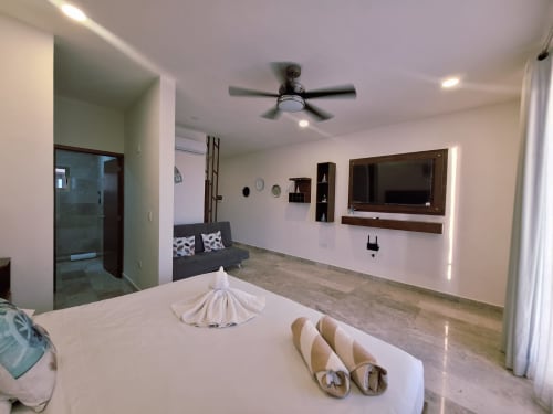 Spacious modern bedroom at Itzamná Suite Deluxe in Playa del Carmen with king bed, flat-screen TV, sitting area, and ceiling