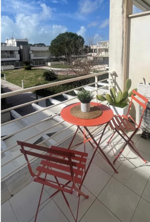 Balcón soleado con sillas rojas, mesa naranja, suculentas en macetas y vistas al jardín en Studio Fregene, Playa Blanca