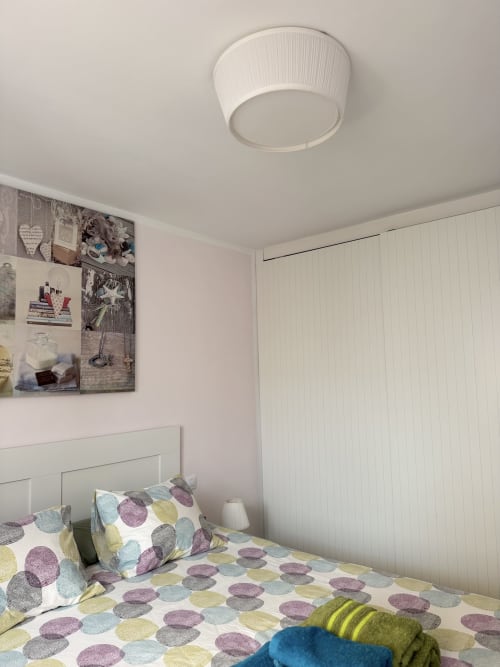 Acogedora habitación en Kamalahouse SL con ropa de cama de patrones coloridos, cabecero blanco, luz de techo y arte decorativo en la pared