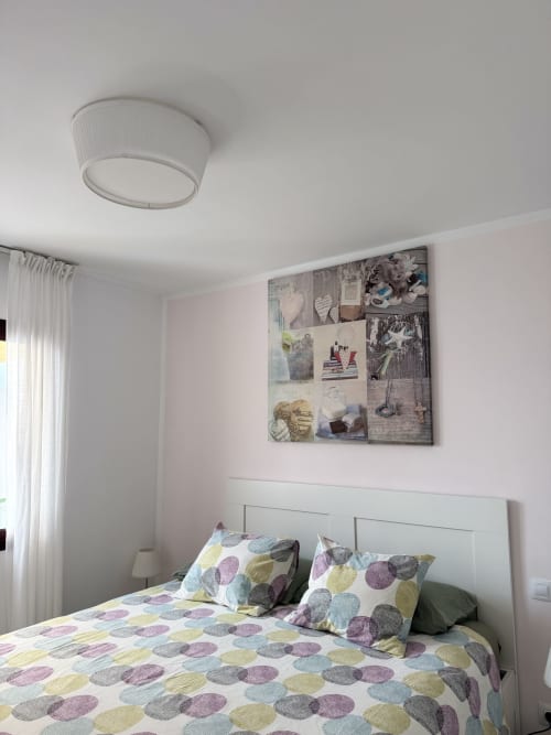 Dormitorio moderno en apartamento Kamalahouse, Corralejo, con ropa de cama colorida, cabecero blanco y pared de galería