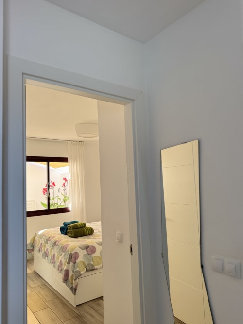 Pasillo luminoso con puerta abierta al dormitorio con flores rosas y toallas azules en Kamalahouse de Corralejo