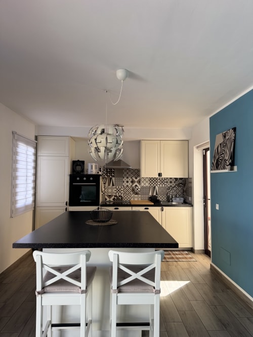 Cocina moderna en apartamento de Corralejo con isla negra, taburetes blancos, armarios crema y pared de acento turquesa