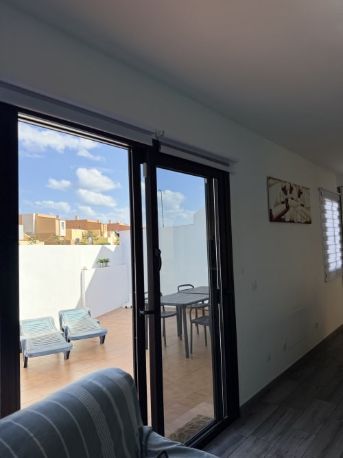 Patio moderno del apartamento en Kamalahouse de Corralejo con tumbonas, mesa de comedor y vistas a la ciudad a través de puertas de cristal