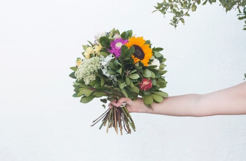 Main tenant un bouquet de fleurs colorées avec tournesol et verdure à l'Hôtel De La Sage