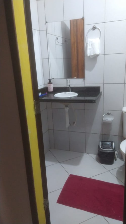 Banheiro moderno com móvel preto, pia redonda, espelho, toilete e tapete vermelho no apartamento Casa do Porto em Boipeba