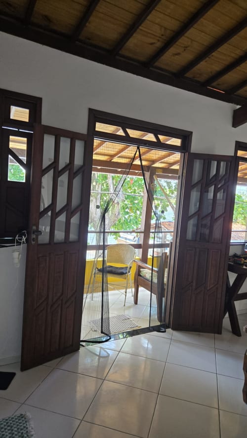 Portas de madeira escura se abrem para pátio à beira-mar com cadeira amarela na Casa do Porto, Boipeba