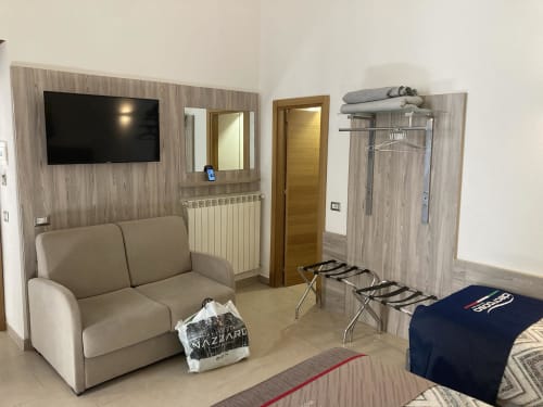 Soggiorno moderno del B&B 4STANZE di Napoli con divano beige, TV schermo piatto, arredi in legno e vista balcone sulla città