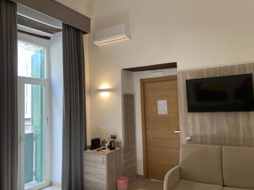 Camera moderna dell'hotel 4STANZE Napoli con balcone, TV a schermo piatto, scrivania in legno e vista sulla città
