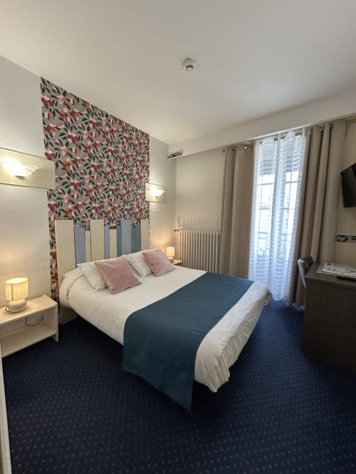 Chambre double moderne à l'Hôtel Le Centre aux Herbiers avec tête de lit fleurie, vue sur la ville, TV et mobilier contemporain