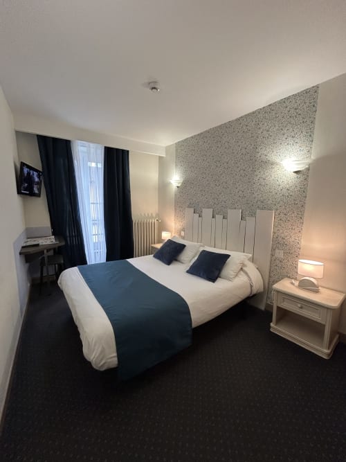 Chambre double moderne à l'Hôtel Le Centre aux Herbiers avec lit, tête de lit blanche, papier peint motifs et vue sur la ville