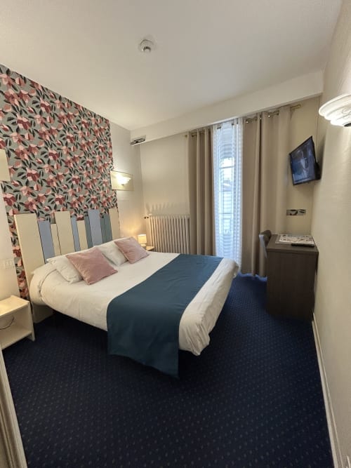 Chambre double de l'Hôtel Le Centre aux Herbiers avec lit queen-size, tête de lit fleurie, vue sur la ville et équipements modernes