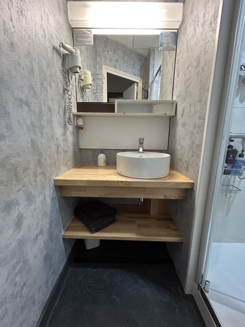 Modern bathroom vanity at Hotel Le Centre with round white sink, wooden countertop, and mirror in Les Herbiers