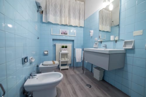 Bright bathroom at Belvedere del Lago with light blue tiled walls, white sink, bidet, toilet, and wooden flooring in