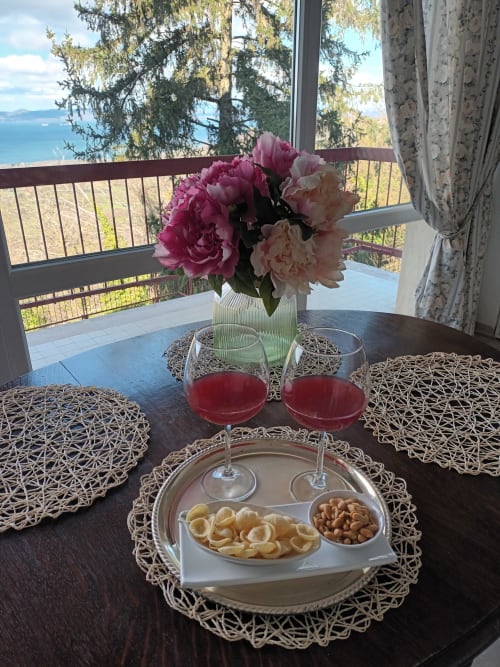 Elegant lakeside dining setup at Belvedere del Lago with pink peonies, red wine glasses, snacks, and Montefiascone lake view