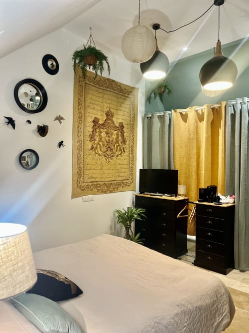 La Secrète bedroom at La Maison d'Horbé with bed, black dresser, desk with TV, hanging pendant lights, and yellow curtains in