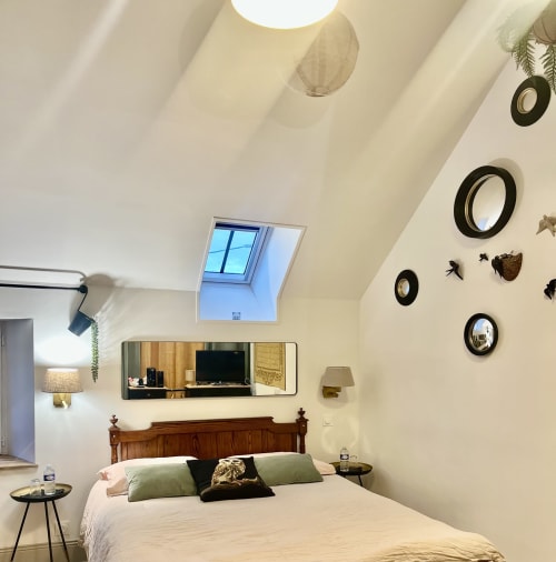 Chambre mansardée cosy à La Maison d'Horbé avec lucarne, lit en bois, oreillers vert sauge et cercles décoratifs muraux