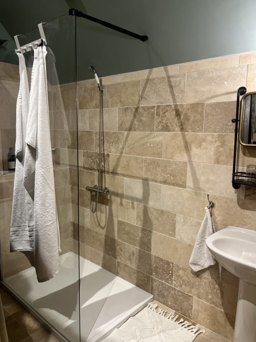 Douche moderne aux parois vitrées, carrelage beige, serviettes blanches et accessoires chromés dans la chambre de La Maison d'Horbé