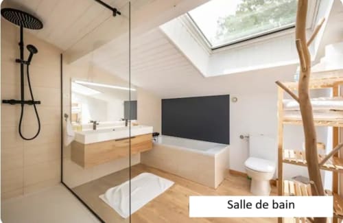 Salle de bains moderne du gîte Le Moulin de Bigorre avec douche italienne, vasque en bois, baignoire balnéo, puits de lumière et toilettes.