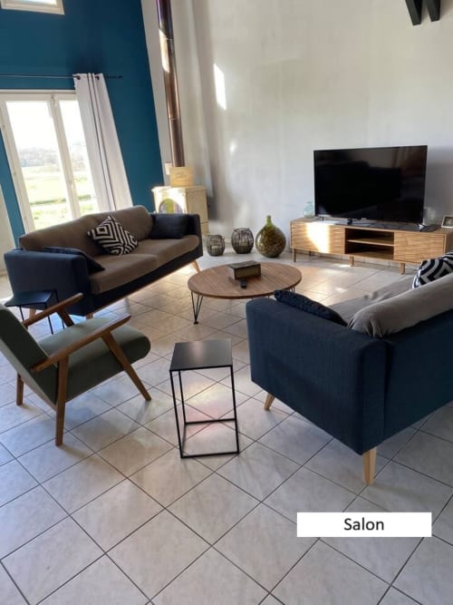Salon moderne du gîte Le Moulin de Bigorre avec mur accent bleu-vert, mobilier confortable, meuble TV en bois et jardin