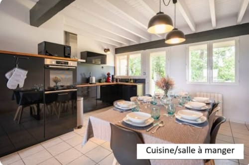 Cuisine-salle à manger moderne du gîte Le Moulin de Bigorre avec électroménagers noirs, poutres blanches, suspensions et table dressée