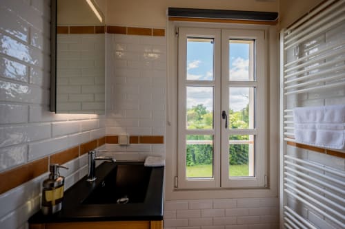 Salle de bain moderne du gîte La Grande Mauvilla avec carrelage blanc métro, lavabo noir et vue sur le jardin par portes-fenêtres