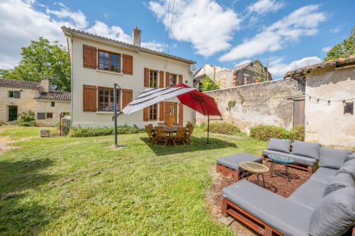 Vaste terrasse de jardin du gîte La Grande Mauvilla avec coin détente et parasol rouge, Civrac-sur-Dordogne