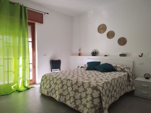 Camera luminosa al Mappamondi B&B di Porticello con biancheria beige a motivi, tende verde lime e decori murali intrecciati