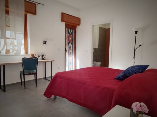 Camera da letto Mappamondi B&B a Porticello con letto rosso, scrivania e porta del bagno in camera