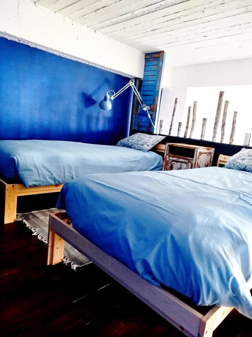 Bright loft bedroom with blue accent wall, two wooden-frame beds with blue bedding, white ceiling beams, and adjustable lamp