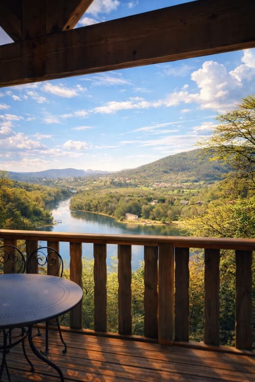 Terrazza in legno con tavolo che si affaccia sulla valle del fiume Ain e sulle montagne boscose delle Cabanes et lodges du Belvédère