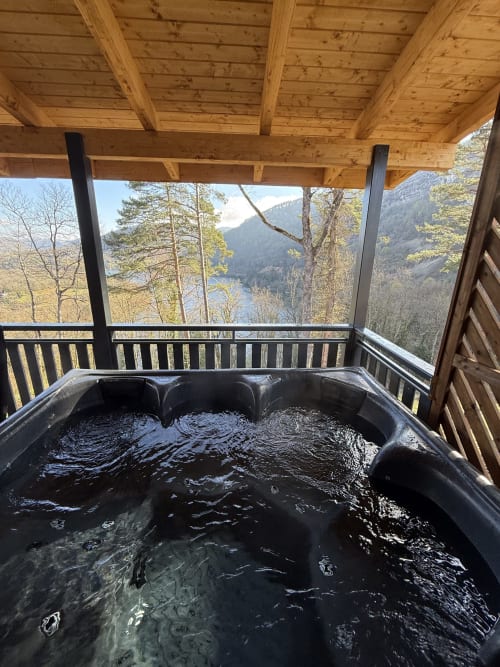 Bain à remous noir sur terrasse en bois dominant le lac de montagne au lodge Cabanes du Belvédère à Serrières-sur-Ain