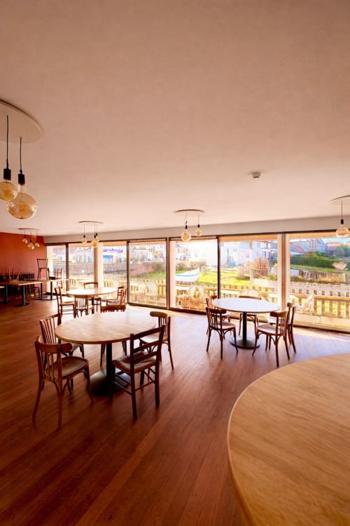Bright dining room at Hôtel de la Plage Wissant with round tables, wooden chairs, and panoramic windows overlooking coastal