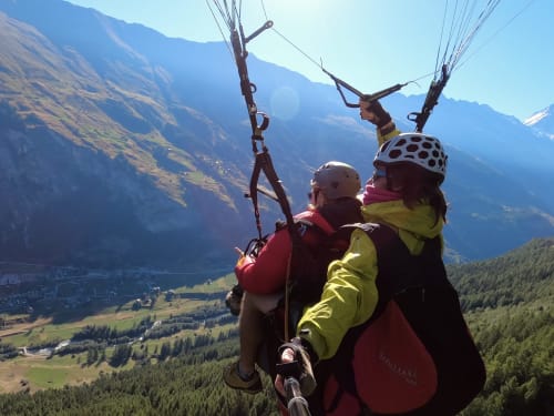 Vol en parapente biplace au-dessus de la vallée de La Sage avec montagnes alpines et paysage forestier