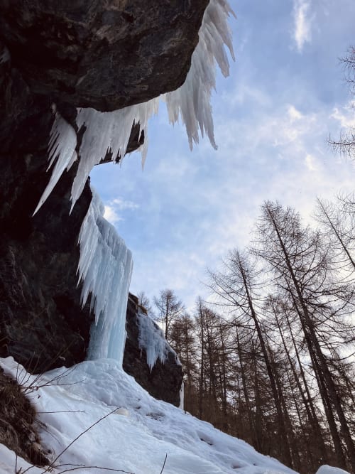 Cascade gelée dégringolant une falaise rocheuse, sol enneigé et mélèzes nus à l'Hôtel De La Sage, La Sage