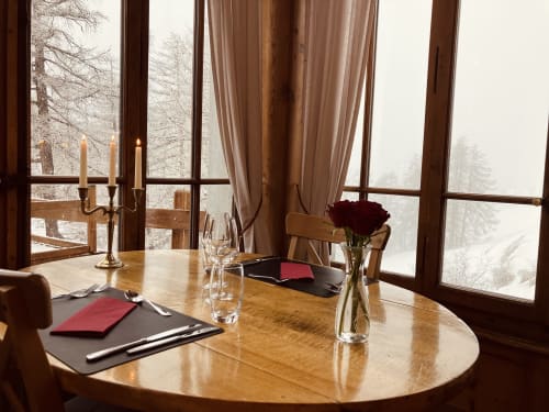 Élégante salle à manger de l'Hôtel De La Sage avec table ronde en bois, roses rouges, lumière de chandelles et vue sur les montagnes enneigées