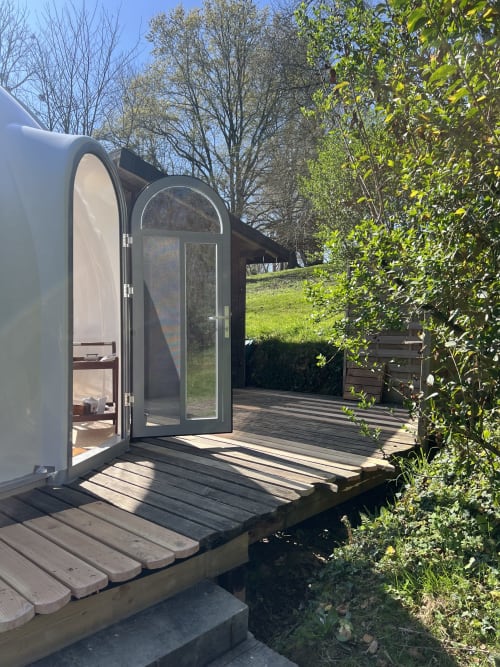 Entrée de la bulle de verre incurvée moderne du Domaine Des Laminak avec terrasse en bois et vue sur le jardin à Bidache, France