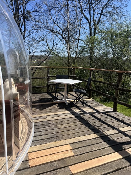 Caravane Airstream sur terrasse en bois avec table et chaises blanches dominant la forêt au Domaine Des Laminak, Bidache