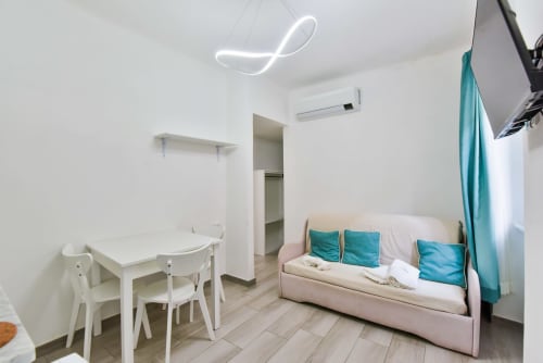 Moderno monolocale a Varigotti con tavolo da pranzo bianco, divano letto rosa con cuscini turchesi, luce al neon e aria condizionata