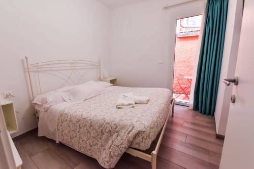 Camera da letto moderna nell'appartamento di Varigotti con letto in ferro bianco, biancheria con motivi, pareti rosa e pavimento in cotto