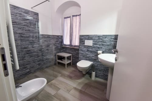 Bagno moderno nell'appartamento VARIGOTTI FABIO con piastrelle scure, sanitari bianchi e finestra ad arco