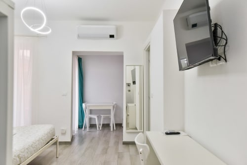 Moderno appartamento a Varigotti con luce neon, letto, scrivania, TV, climatizzatore e pavimento in legno in interno bianco luminoso