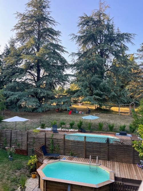Above-ground pool at Domaine le Manoir with wooden deck, fencing, and majestic cedars in Fossemagne, France